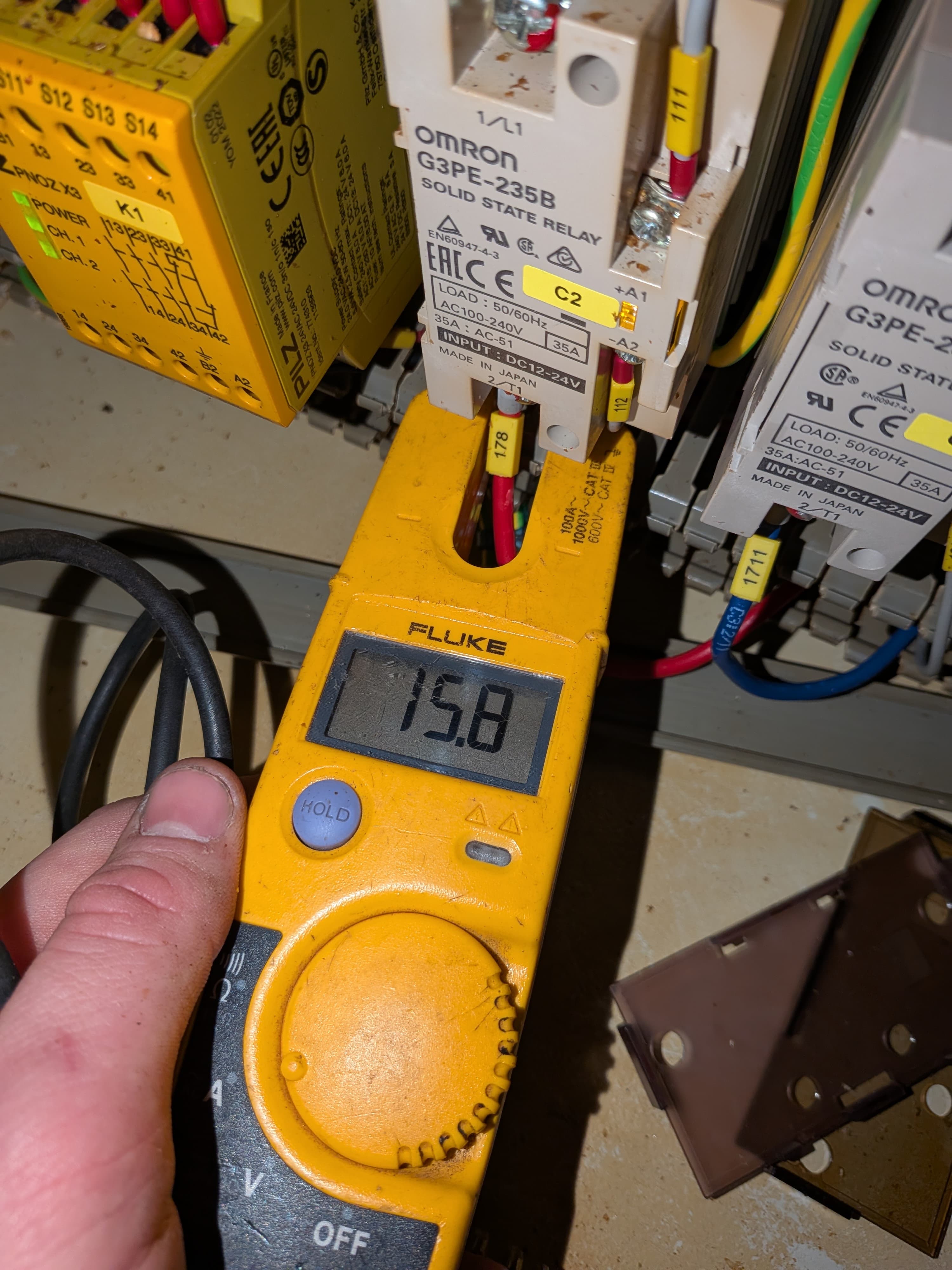A Fluke multimeter taking a reading at a control panel, in front of solid-state relays and a safety relay